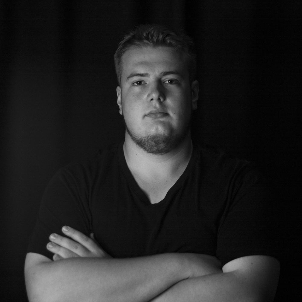 Portrait of the engineer with arms crossed, lit from one side against a black background.
